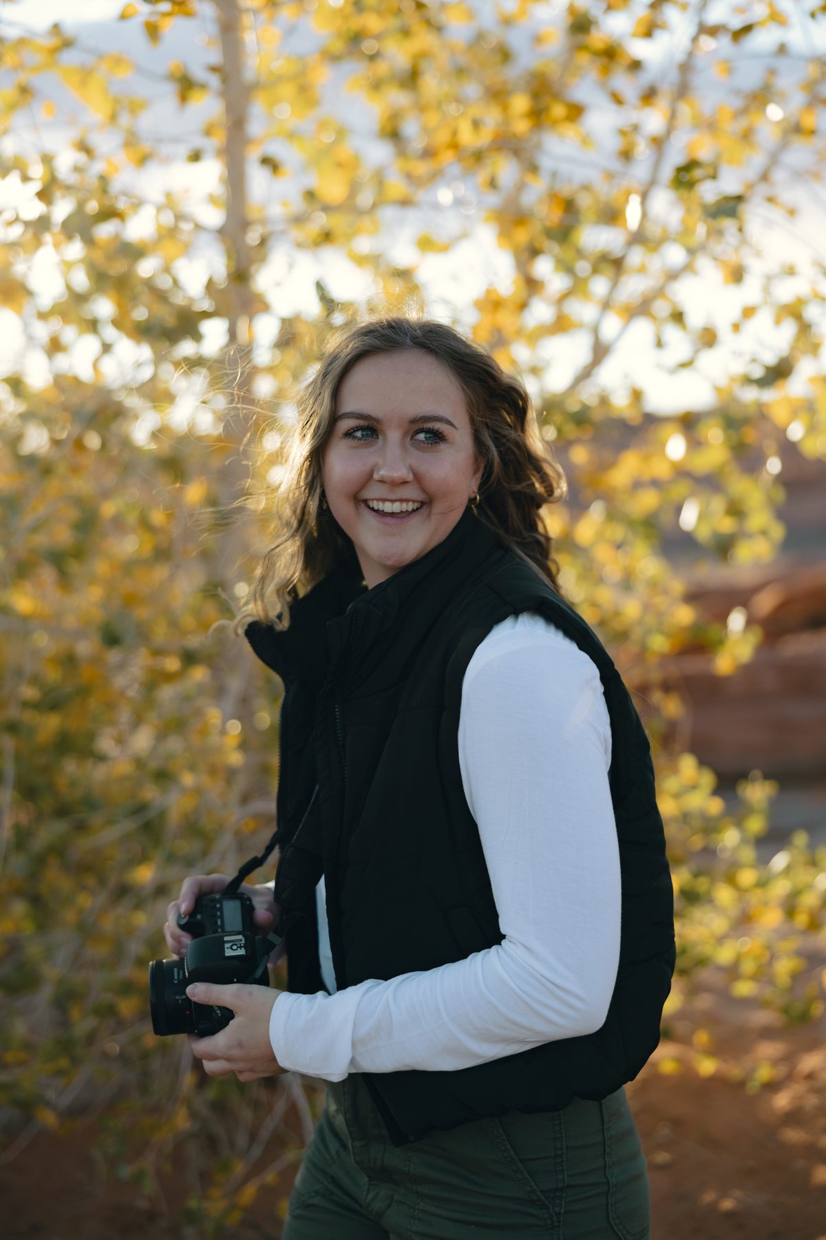 Sydney smiling, holding her camera in a golden aspen grove