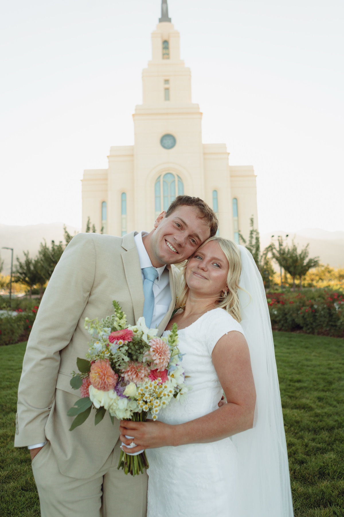 Bride and groom embracing in front of a temple at golden hour, bride holding a colorful bouquet
